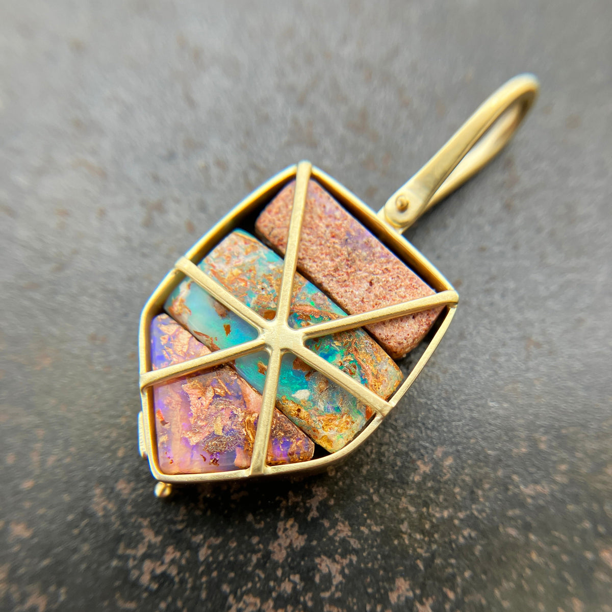 A shield-shaped pendant featuring an 18k gold frame and three rectangular inlay wood replacement opals in pink, turquoise, purple, and brown.