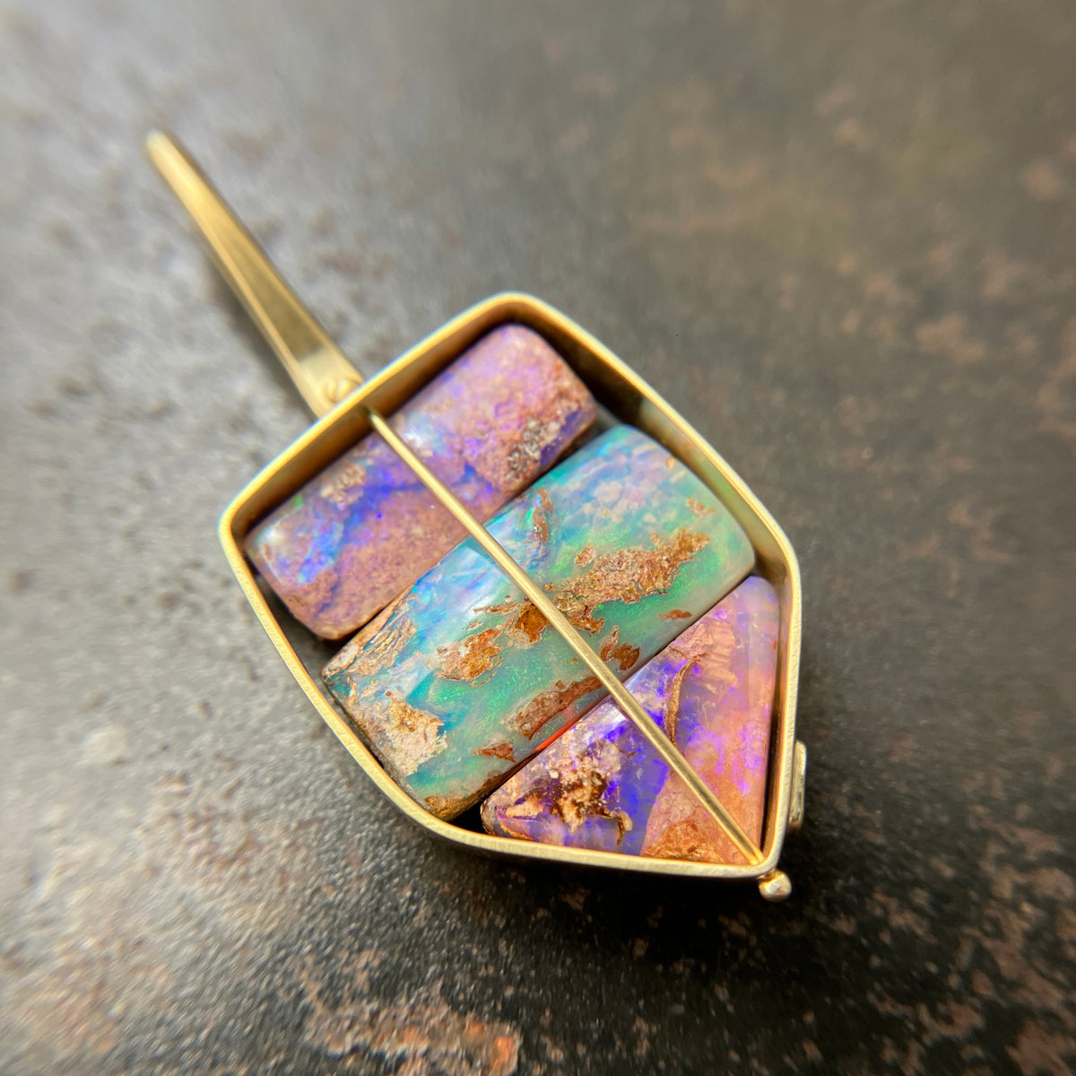 A shield-shaped pendant featuring an 18k gold frame and three rectangular inlay wood replacement opals in pink, turquoise, purple, and brown.