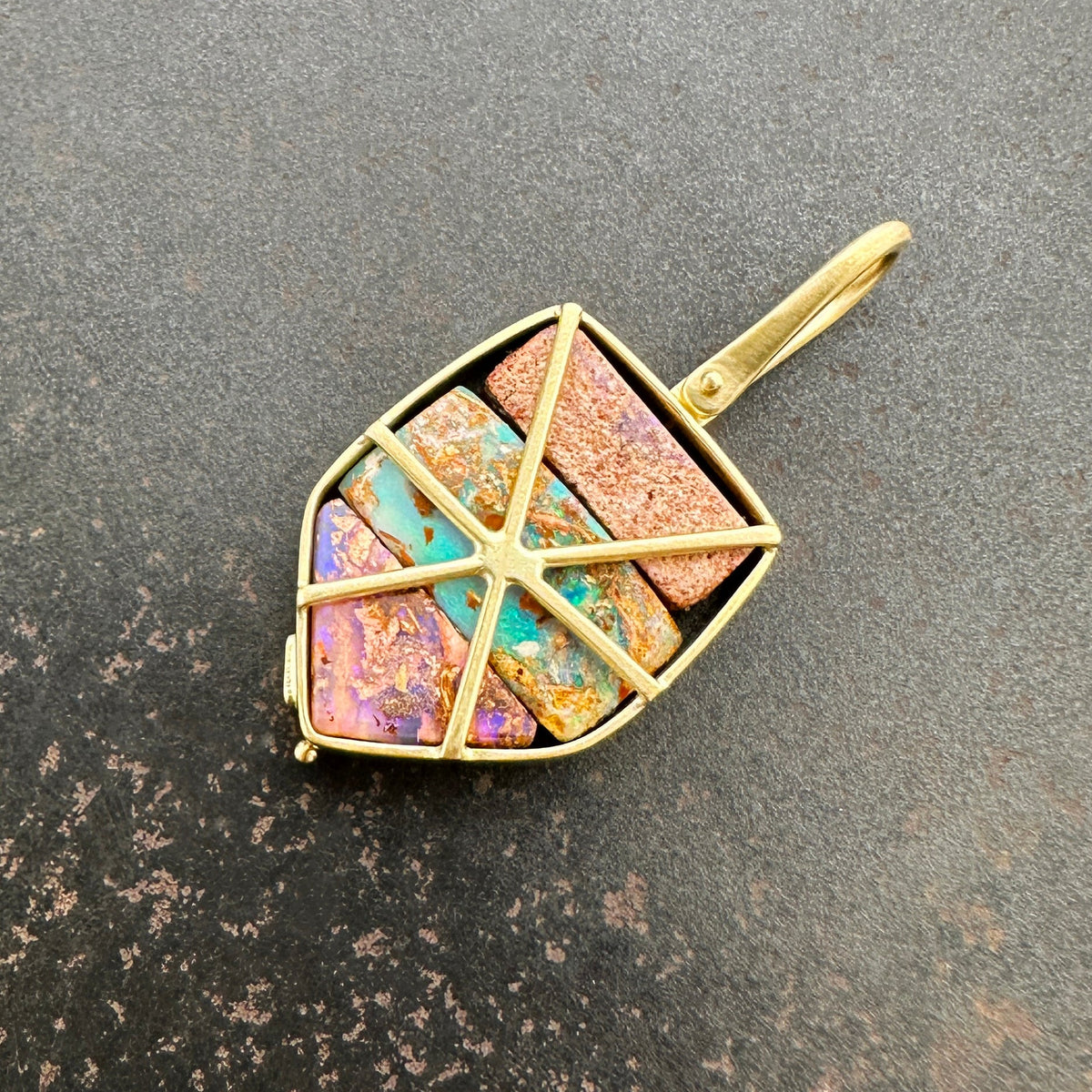 A shield-shaped pendant featuring an 18k gold frame and three rectangular inlay wood replacement opals in pink, turquoise, purple, and brown.