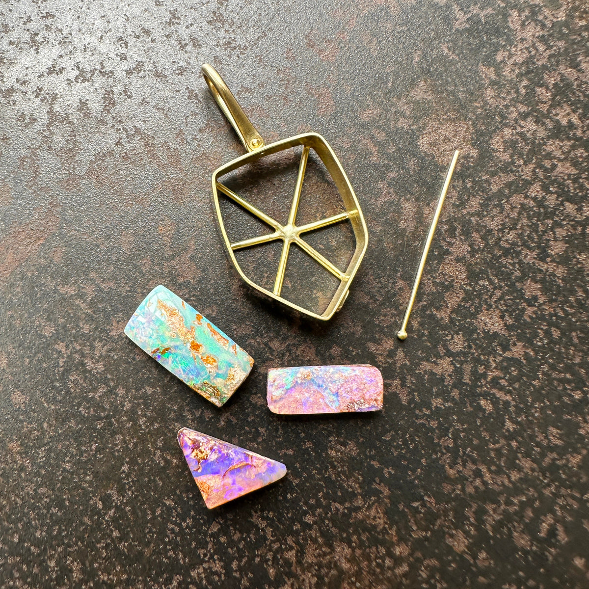 A shield-shaped pendant featuring an 18k gold frame and three rectangular inlay wood replacement opals in pink, turquoise, purple, and brown.