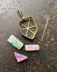A shield-shaped pendant featuring an 18k gold frame and three rectangular inlay wood replacement opals in pink, turquoise, purple, and brown.