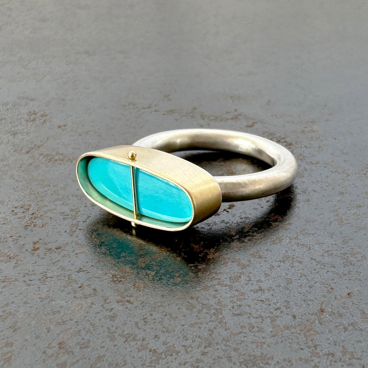 Silver and gold ring with a turquoise stone on a gray surface