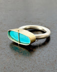 Silver and gold ring with a turquoise stone on a gray surface