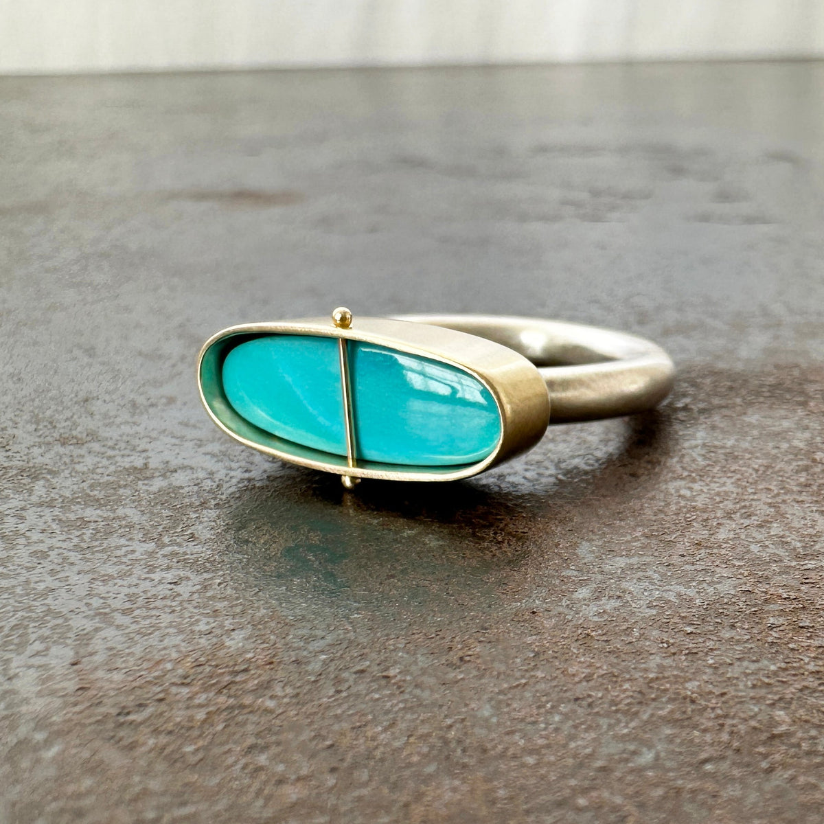 Silver and gold ring with a turquoise stone on a gray surface