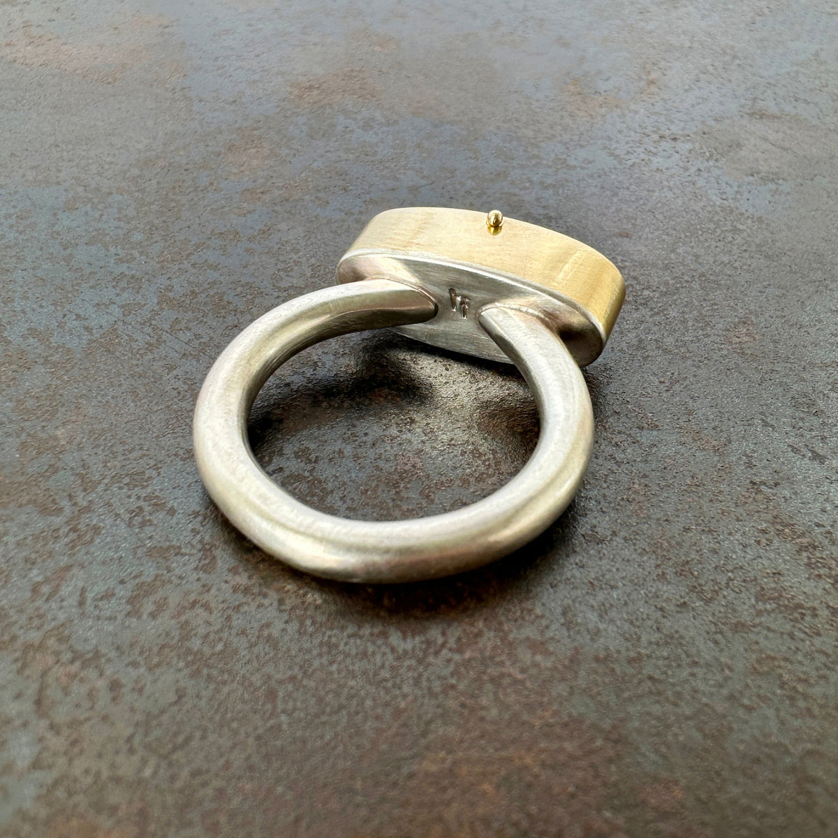 Silver and gold ring with a turquoise stone on a gray surface