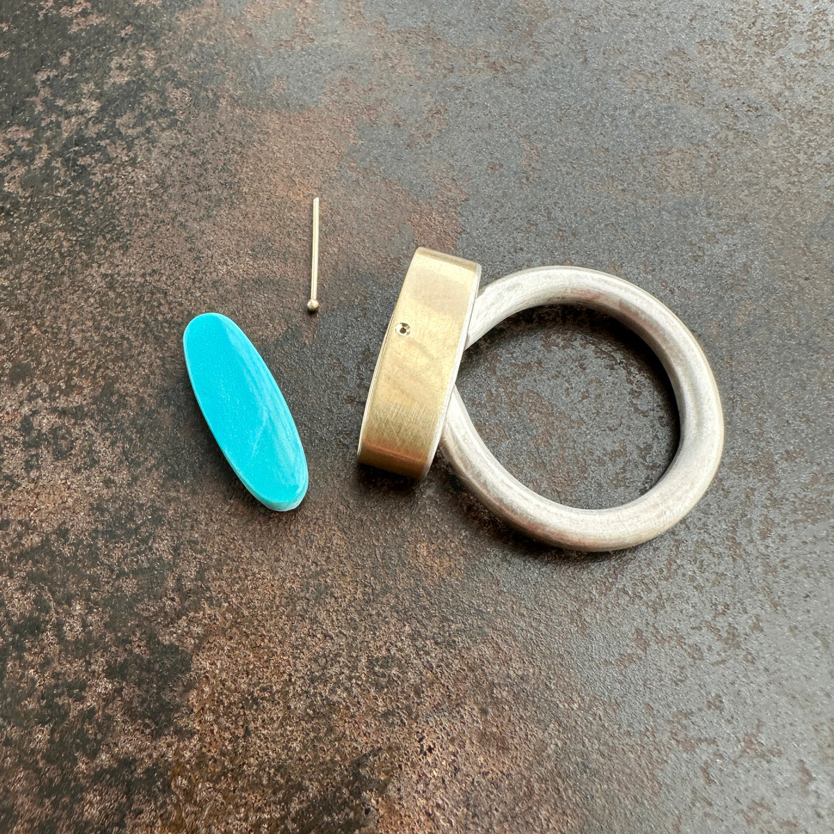 Silver and gold ring with a turquoise stone on a gray surface