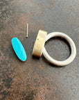 Silver and gold ring with a turquoise stone on a gray surface