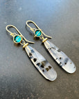Pair of earrings with teardrop-shaped montana agates and turquoise with 18k gold on a textured gray background